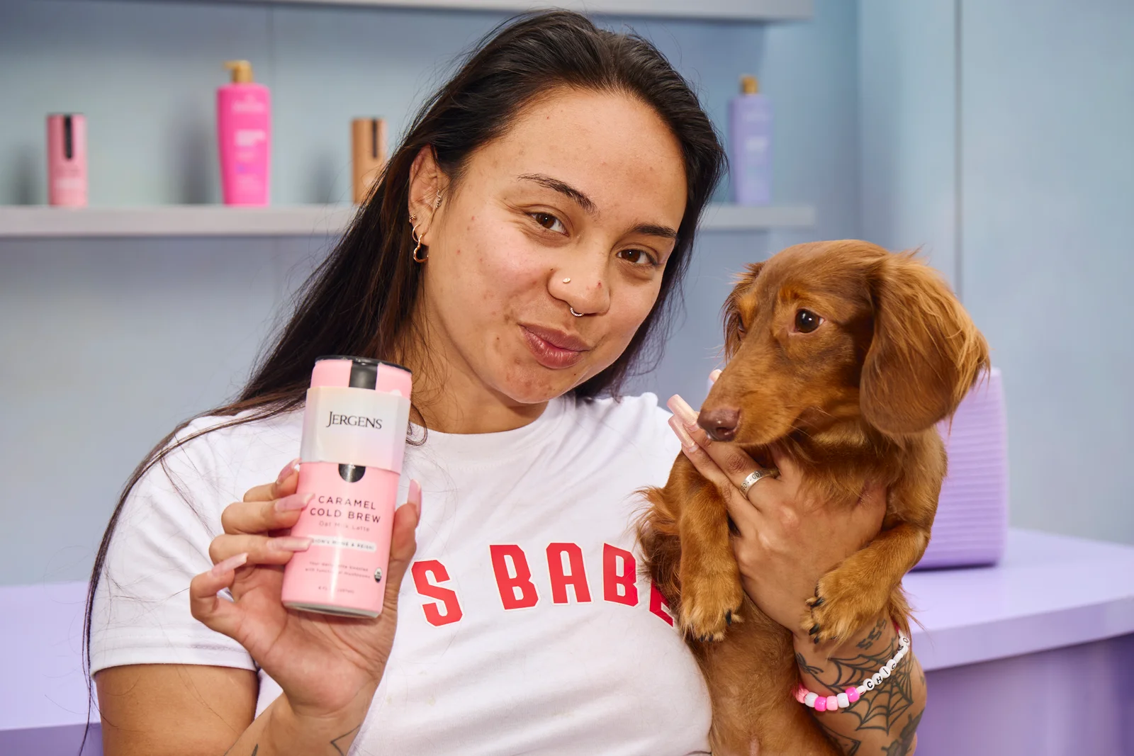 A creator holding a Jergens lotion with her dachshund on the pastel set of a brand activation