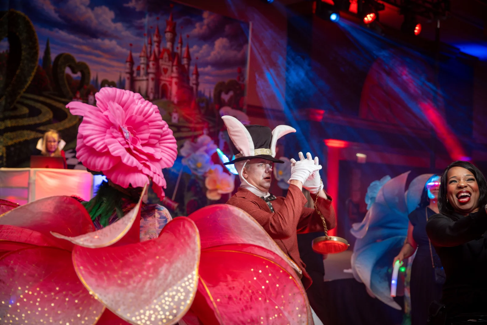 A costumed performer and a laughing guest at a Wonderland-themed gala, under the stage lights