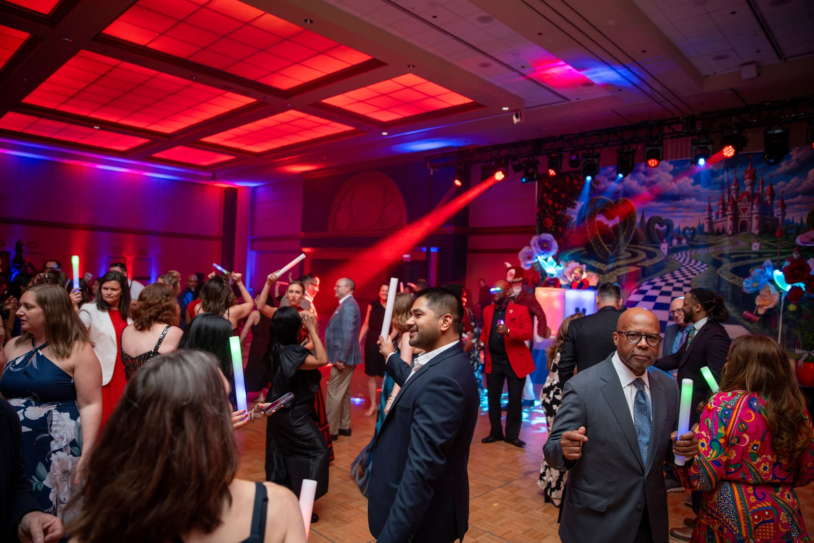 Guests dancing with glow sticks on a gala floor under red lights
