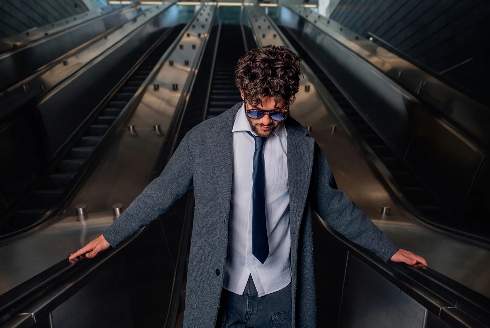 Editorial portrait of a man in a coat and tie between two escalators